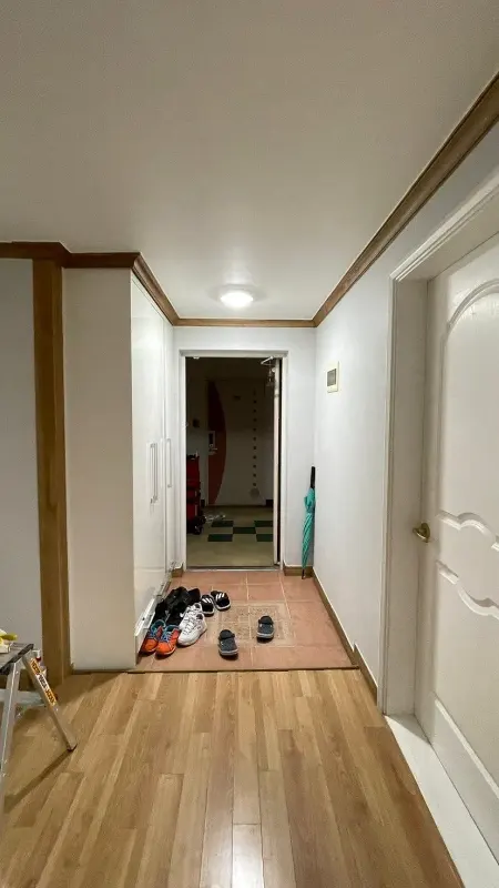 왼편에 흰색 신발장이 있는 시공 전 아파트 현관과 복도