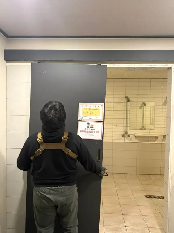 작업자가 레일에서 빠진 회색 문짝을 붙잡고 상태를 살피는 모습