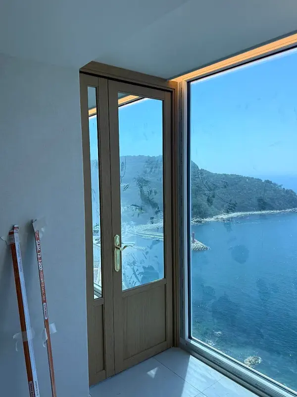 바다가 보이는 통창 옆에 세워진 피넛오크 색 스윙 중문