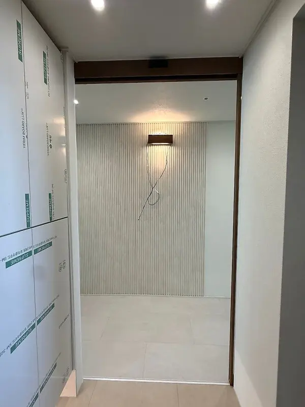 자동 중문이 열려 현관 안쪽 벽등과 타일 벽이 보이는 모습